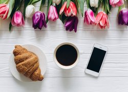 Kawa obok rogalika i telefonu oraz tulipanów