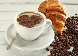 Kawa udekorowana czekoladową posypką w kształcie serca i croissant