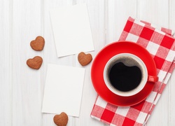 Kawa w czerwonej filiżance obok karteczek i serduszkowych ciasteczek