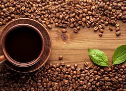 Kawa w filiżance i zielone listki pomiędzy ziarnami kawy