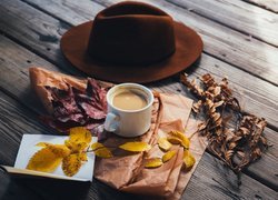 Kawa w filiżance na deskach obok kapelusza i jesiennych liści