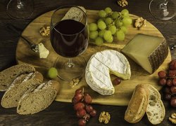 Kieliszek wina obok serów i winogron na desce