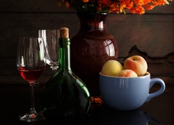 Kieliszki z winem obok butelki i filiżanki z brzoskwiniami