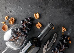 Kiść ciemnych winogron w kieliszku i butelka wina obok scyzoryka