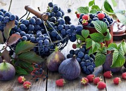 Kiście winogron w koszyczku obok fig i malin na deskach