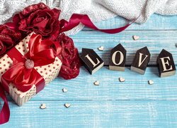 Klocki z napisem Love obok prezentu i sztucznych róż