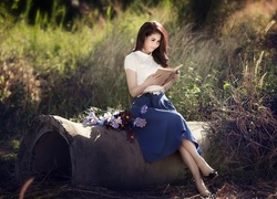 Kobieta czyta książkę siedząc na betonowej rurze