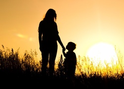 Kobieta i dziecko na łące oglądają zachód słońca