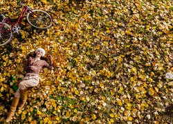 Kobieta leżąca obok roweru na opadłych liściach