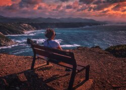 Kobieta na ławce nad morzem o zachodzie słońca