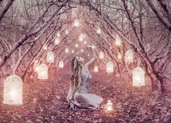 Kobieta otoczona szpalerem drzew oświetlonych lampionami