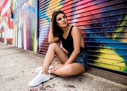 Kobieta siedząca na chodniku pod ścianą z graffiti