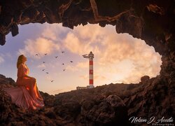 Kobieta siedząca na skałach w jaskini i latarnia morska w tle