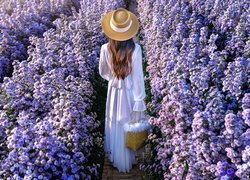 Kobieta w białej sukience na ścieżce wśród niebieskich kwiatów