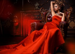 Kobieta w czerwonej sukni odpoczywa w fotelu przy kominku