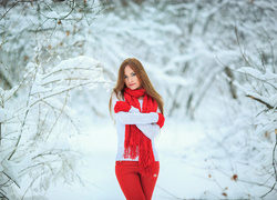 Kobieta w czerwonym szaliku i rękawiczkach pozuje w zimowym lesie