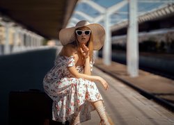 Kobieta w kapeluszu i letniej sukience na peronie