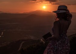 Kobieta w kapeluszu oglądająca zachód słońca nad górami