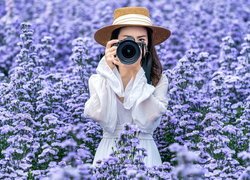 Kobieta w kapeluszu z aparatem fotograficznym wśród niebieskich kwiatów