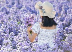 Kobieta w kapeluszu zbierająca niebieskie kwiaty