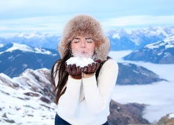 Kobieta w zimowej czapce i rękawiczkach zdmuchuje śnieg z dłoni
