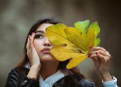 Kobieta z jesiennymi liśćmi przy twarzy