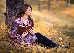 Kobieta z książką na polanie pod drzewem