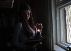 Kobieta z lampą i książką przy oknie