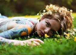 Kobieta z tatuażem i wiankiem leżąca na trawie