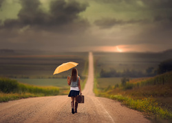 Kobieta z walizką i parasolem idąca drogą
