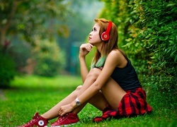 Kobieta ze słuchawkami na uszach siedzi na zielonej trawie