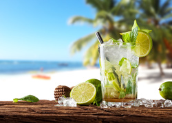 Koktajl alkoholowy mojito i limonki na drewnianym blacie z plażą w tle