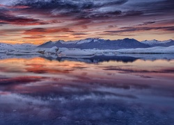 Kolorowe chmury nad zimowymi górami odbijają się w wodzie