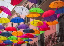 Kolorowe parasolki nad ulicą obok domu z balkonami