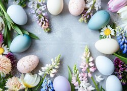 Kolorowe pisanki i różne kwiaty ułożone na jasnoniebieskim tle