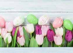 Kolorowe pisanki i tulipany na białych deskach