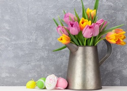 Kolorowe pisanki ze wstążkami obok tulipanów w dzbanku