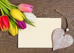 Kolorowe tulipany położone obok kartki i zawieszki z serduszkiem