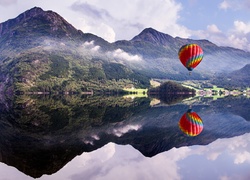 Kolorowy balon i góry spowite mgłą odbijają się w jeziorze