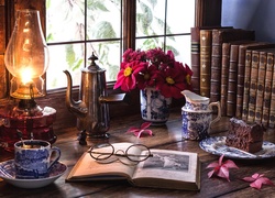 Kompozycja z lampą naftową, książkami, kawą i ciastem na talerzyku