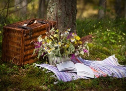 Kosz piknikowy i bukiet polnych kwiatów pod drzewem