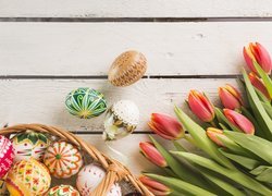 Kosz pisanek obok tulipanów na deskach