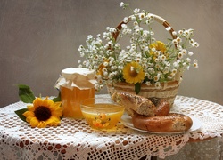 Kosz z kwiatami oraz bułki i miód na stole