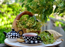 Koszyk z kwiatami lipy obok imbryka i filiżanki z herbatą