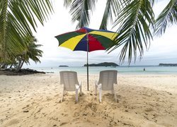 Krzesła pod kolorowym parasolem na plaży