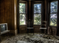 Krzesła pod oknami i telewizor na stoliku w zniszczonym pokoju