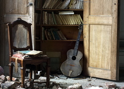 Krzesło i gitara przy regale z książkami w zniszczonym wnętrzu