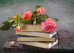 Książki leżące na drewnianym stoliku nakryte różami