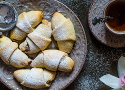 Kubek herbaty obok rogalików posypanych cukrem pudrem