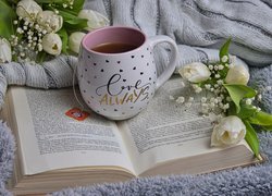 Kubek z herbatą i białe tulipany na książce